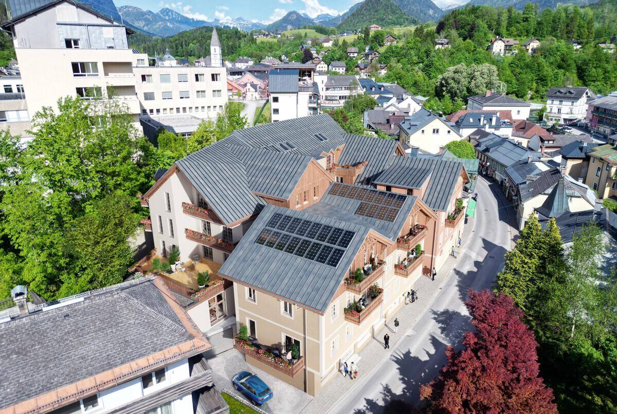 Luftaufnahme eines Gebäudekomplexes mit Solaranlagen auf den Dächern und Balkonen in grüner Umgebung.