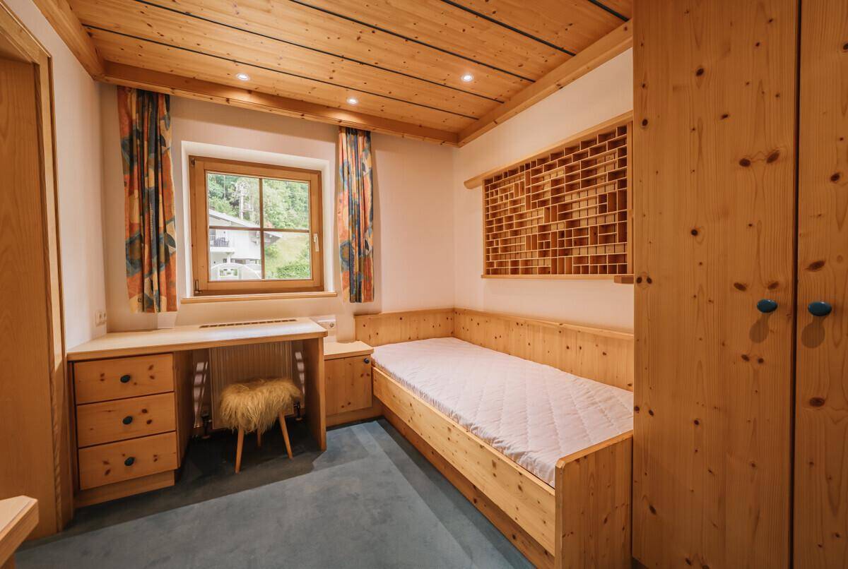 Helles Schlafzimmer mit Einzelbett, Holzmöbeln und Blick ins Grüne, ideal als Gästezimmer.
