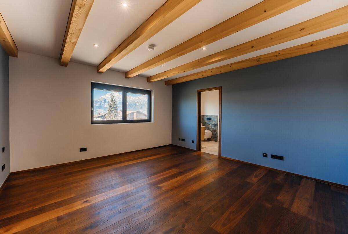 Geräumiges Schlafzimmer mit Holzboden, Holzbalken und Fenster mit Bergblick.
