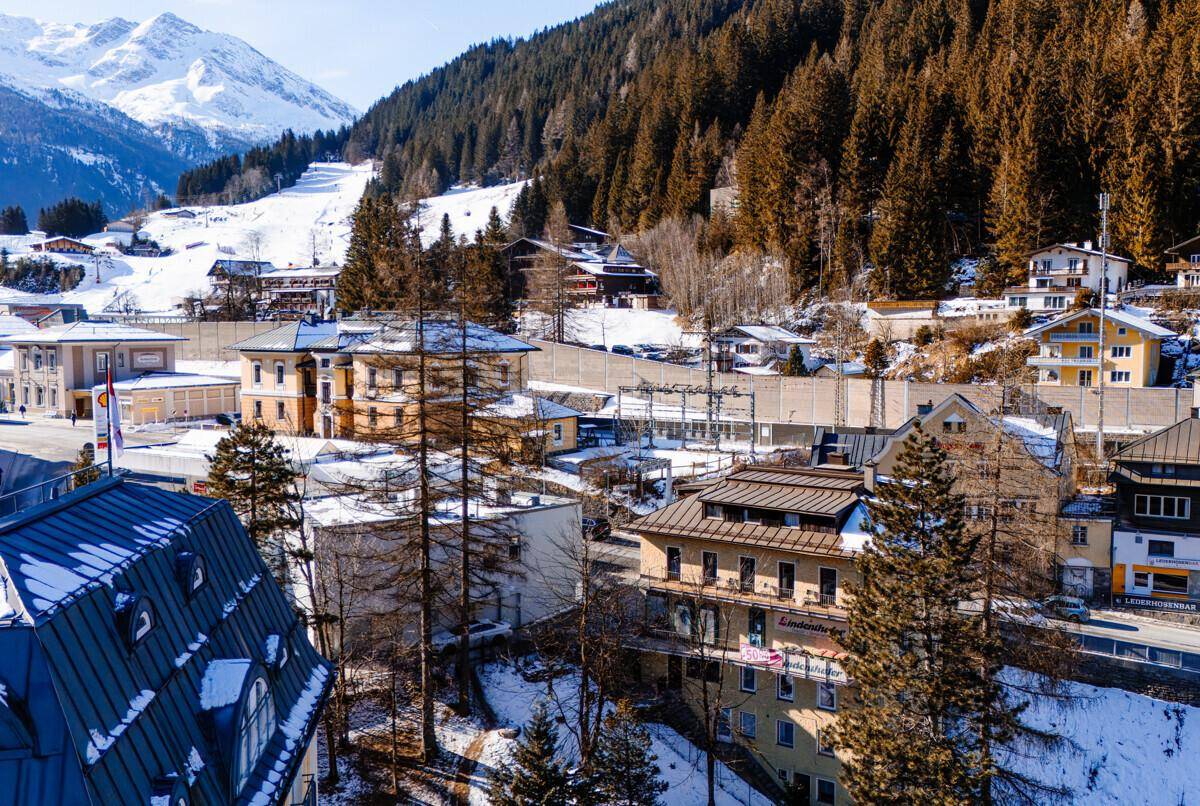 Panoramablick auf eine verschneite Berglandschaft mit Häusern und Skipisten im Hintergrund.
