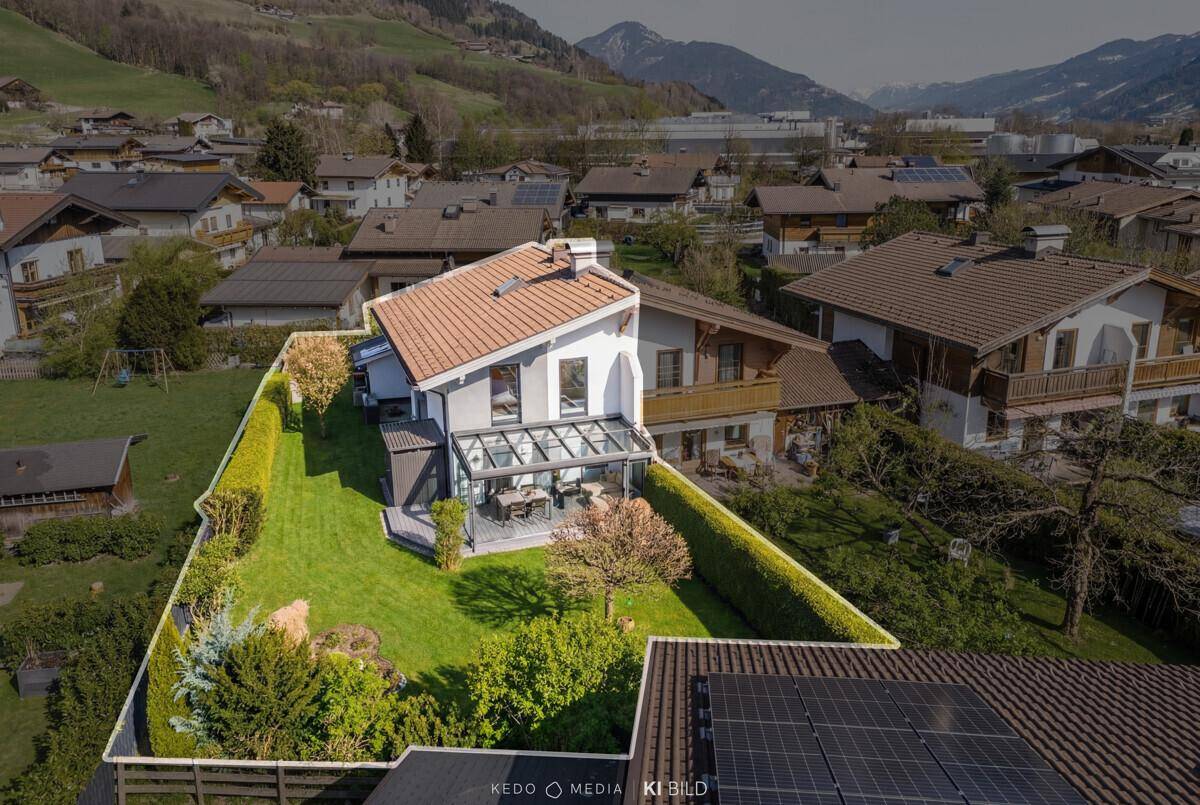 Luftaufnahme des Hauses mit großem Garten und umliegender Wohnbebauung in bergiger Landschaft.