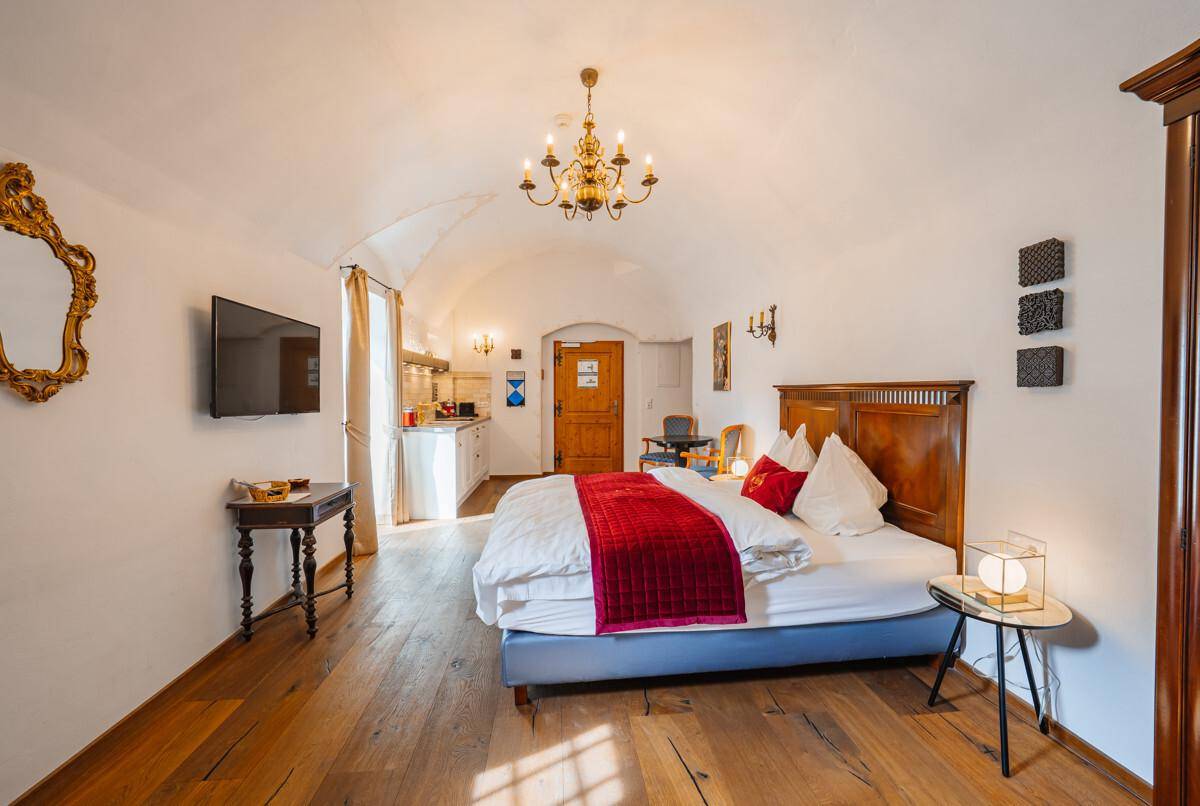 Geräumiges Schlafzimmer mit Gewölbedecke, Holzboden und integrierter Küchenzeile.