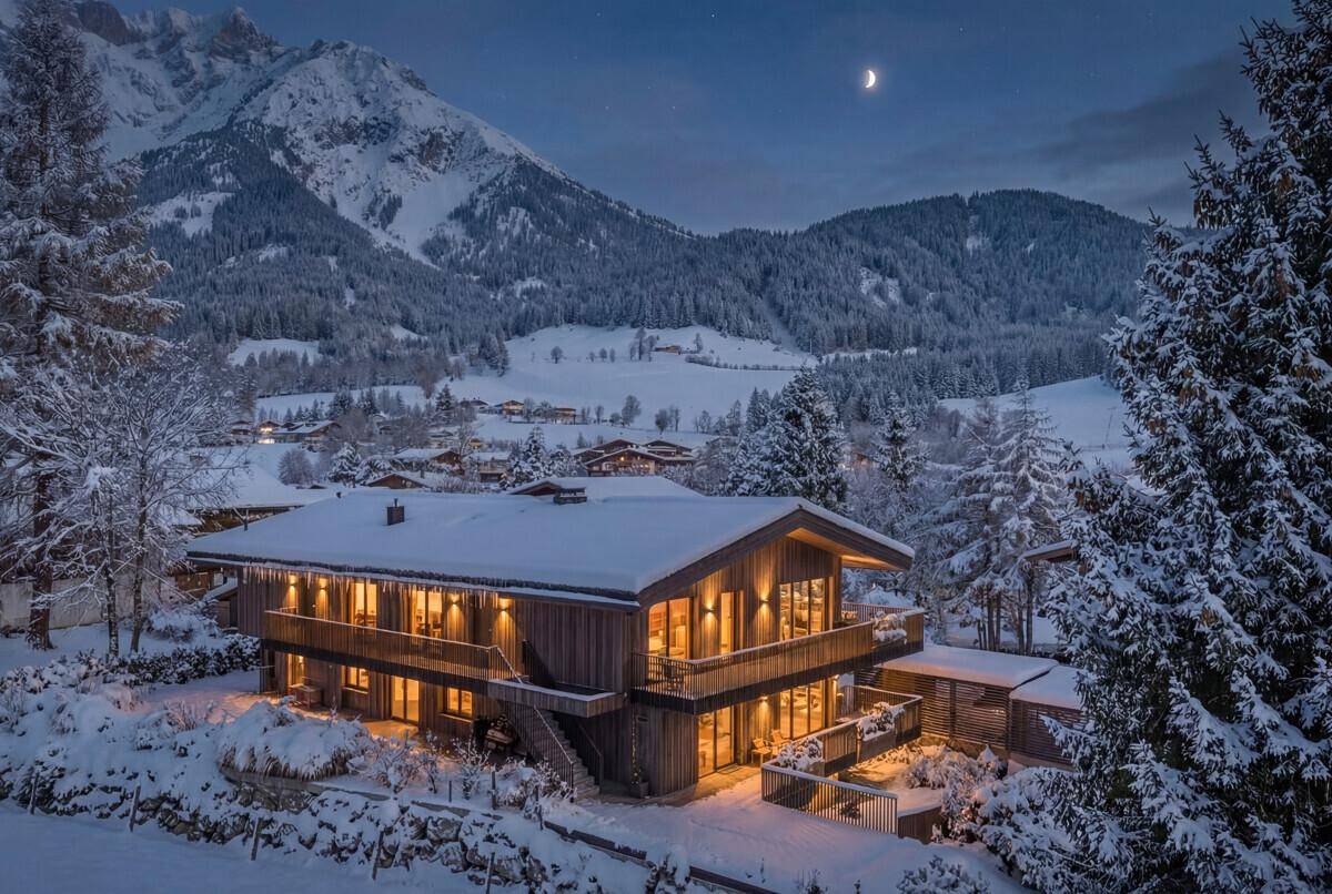 Traditionelles Chalet in verschneiter Winterlandschaft bei Nacht mit beleuchteten Fenstern.