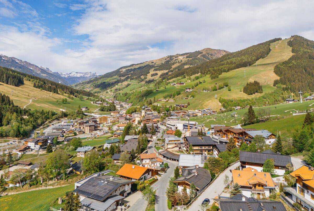 Umfassender Blick auf ein Bergdorf mit Skipisten und grünen Hängen unter blauem Himmel.