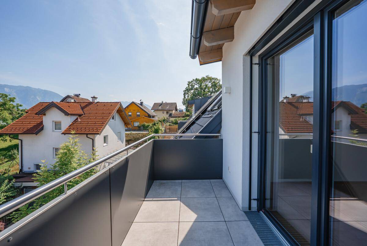 Heller Balkon mit Fliesenboden und Metallgeländer, bietet einen Blick auf Häuser und Berge.
