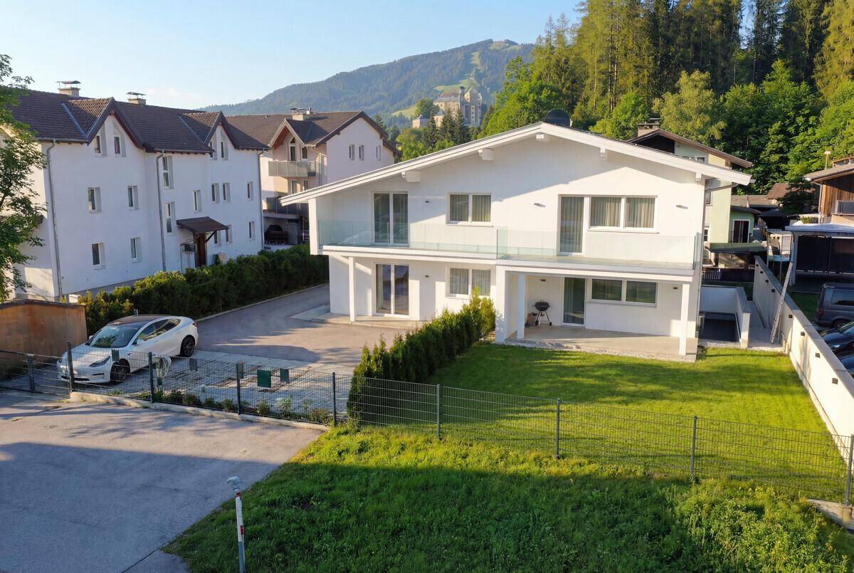 Neubau-Einfamilienhaus mit gepflegtem Vorgarten und Parkplätzen in alpiner Umgebung.