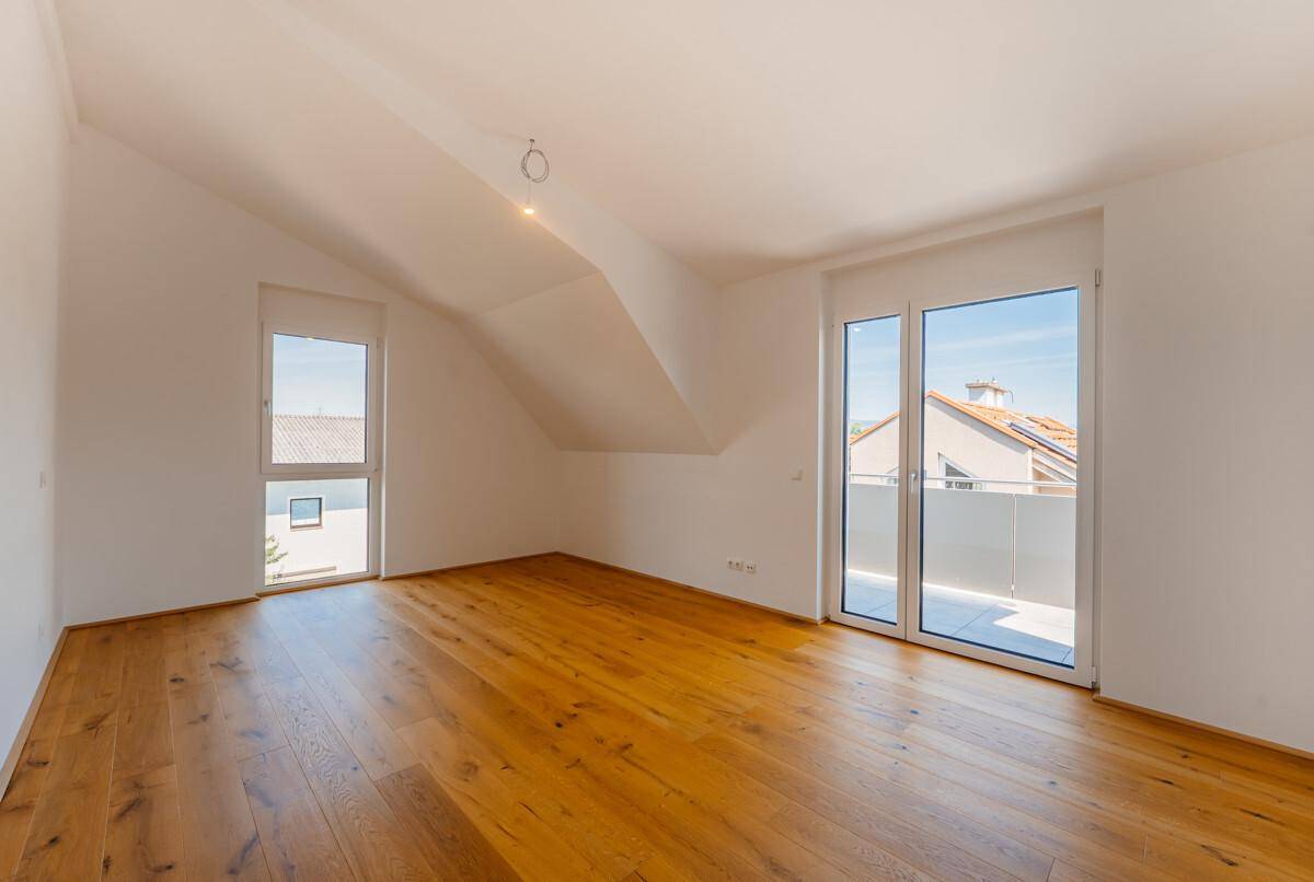 Helles, unmöbliertes Schlafzimmer mit Holzboden, Dachschrägen und Zugang zu einem Balkon oder einer Terrasse.