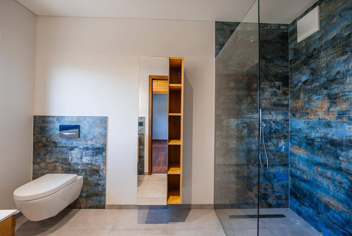 Elegantes Badezimmer mit Wand-WC, begehbarer Dusche und blauen Akzentfliesen.