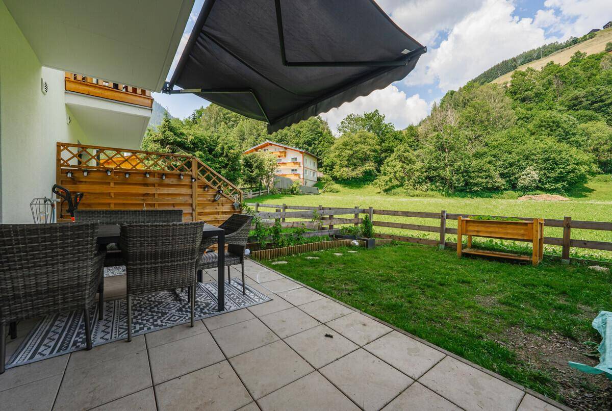 Gemütliche Terrasse mit Gartenmöbeln, Rasenfläche und Blick auf die umliegende grüne Landschaft.