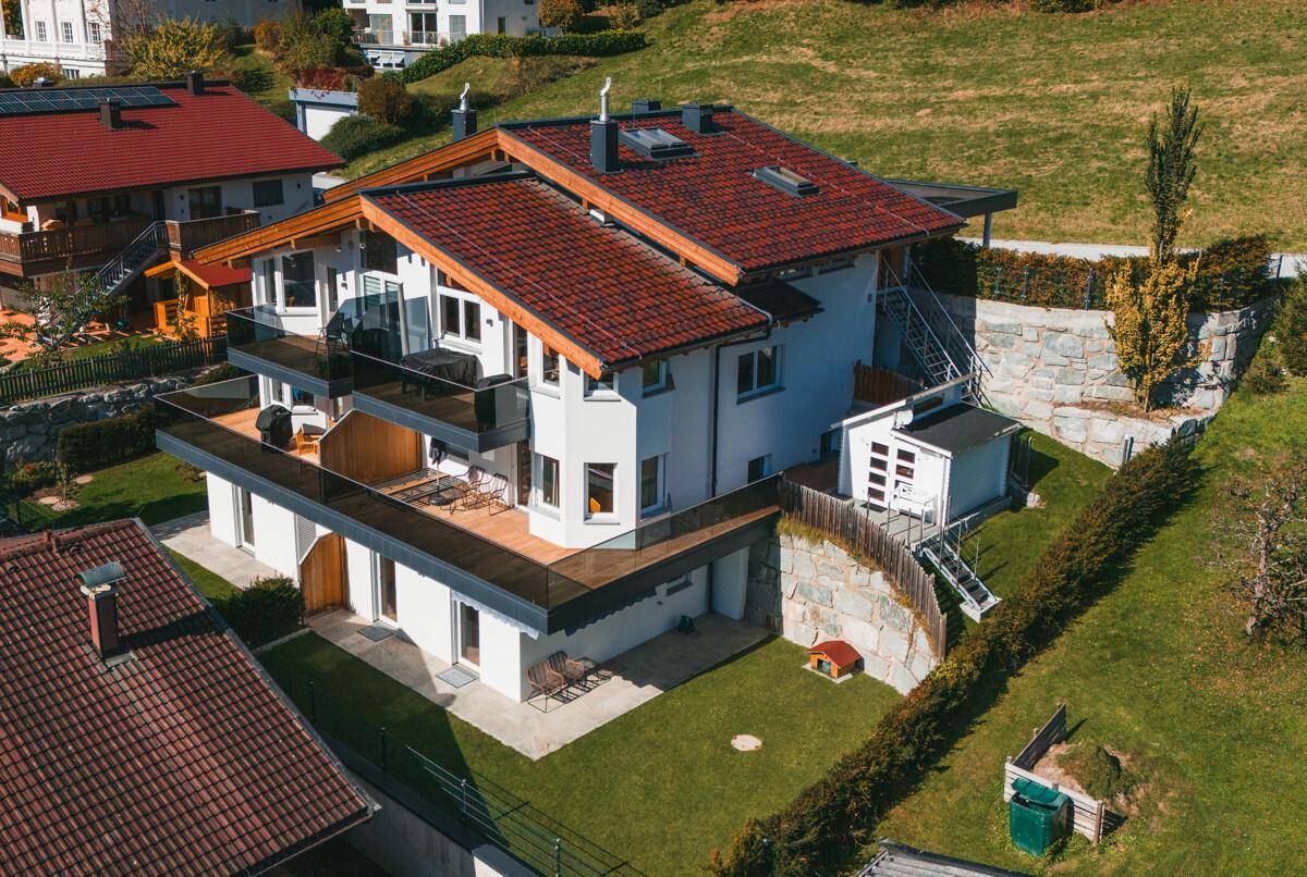 Modernes Wohnhaus mit mehreren Balkonen und Terrassen in Hanglage mit umliegender Grünfläche.
