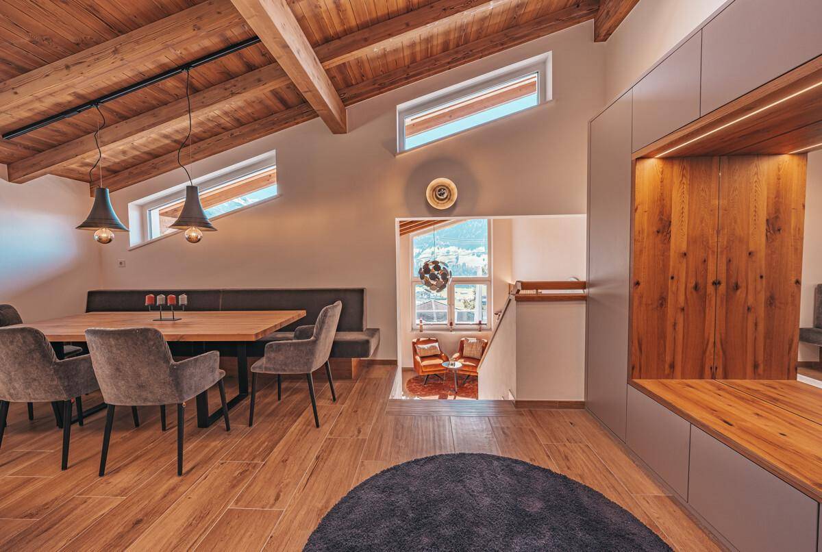 Essbereich mit großem Holztisch, Sitzbank und Blick auf den Wohnbereich und die Treppe.