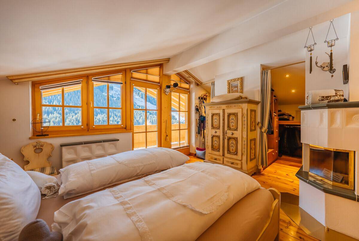 Gemütliches Schlafzimmer mit Kachelofen, Holzboden und großen Fenstern mit Bergblick.