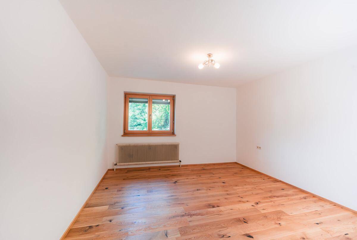 Leeres Zimmer mit Holzboden und Fenster, das viel natürliches Licht hereinlässt.