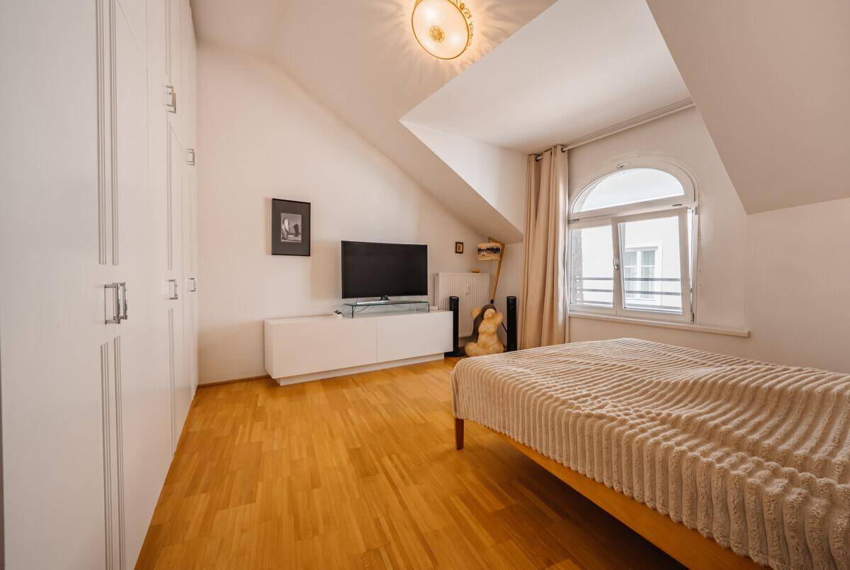 Gemütliches Schlafzimmer im Dachgeschoss mit Holzboden, Einbauschränken und schrägem Dach.