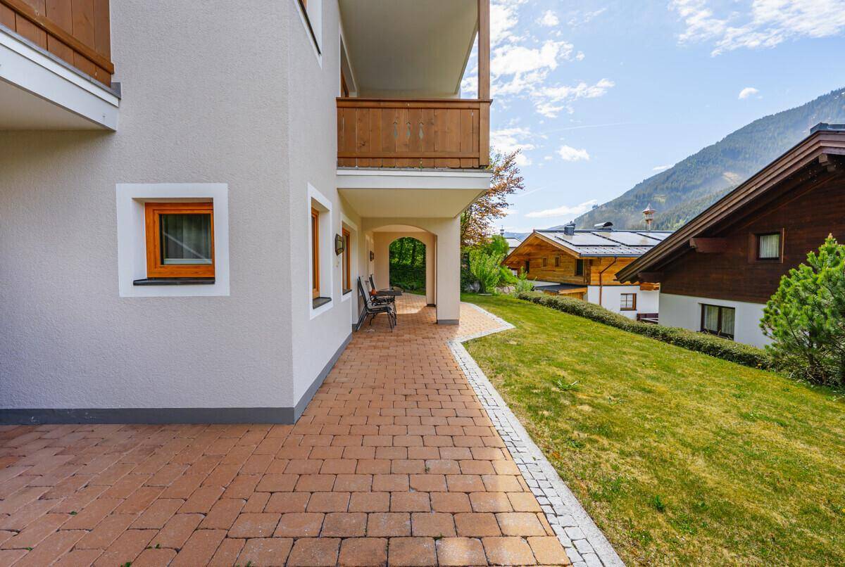 Gepflasterte Terrasse neben dem Gebäude mit Rasenfläche und Bergblick.