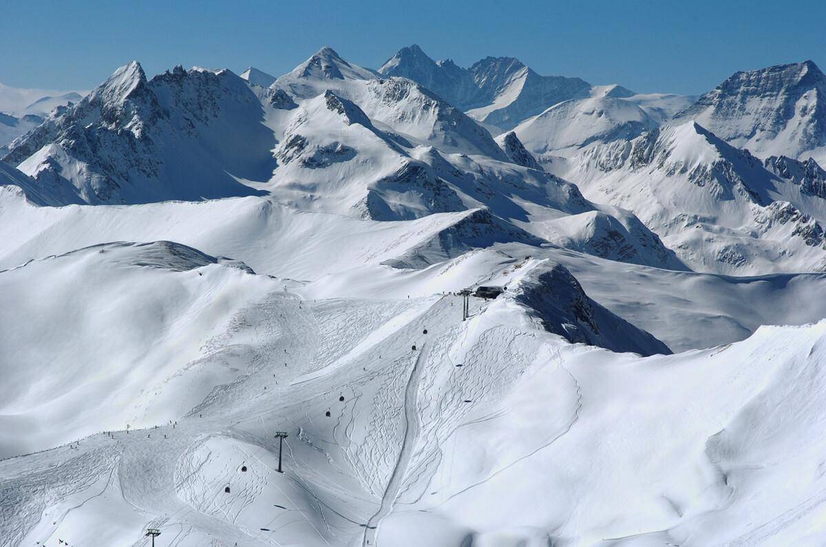 Atemberaubende Winterlandschaft mit weiten Schneefeldern, Skipisten und majestätischen Berggipfeln.