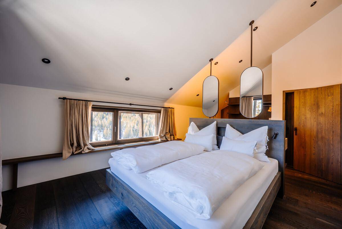 Helles Schlafzimmer mit Doppelbett, Holzboden und Fenster mit Blick auf die Natur.