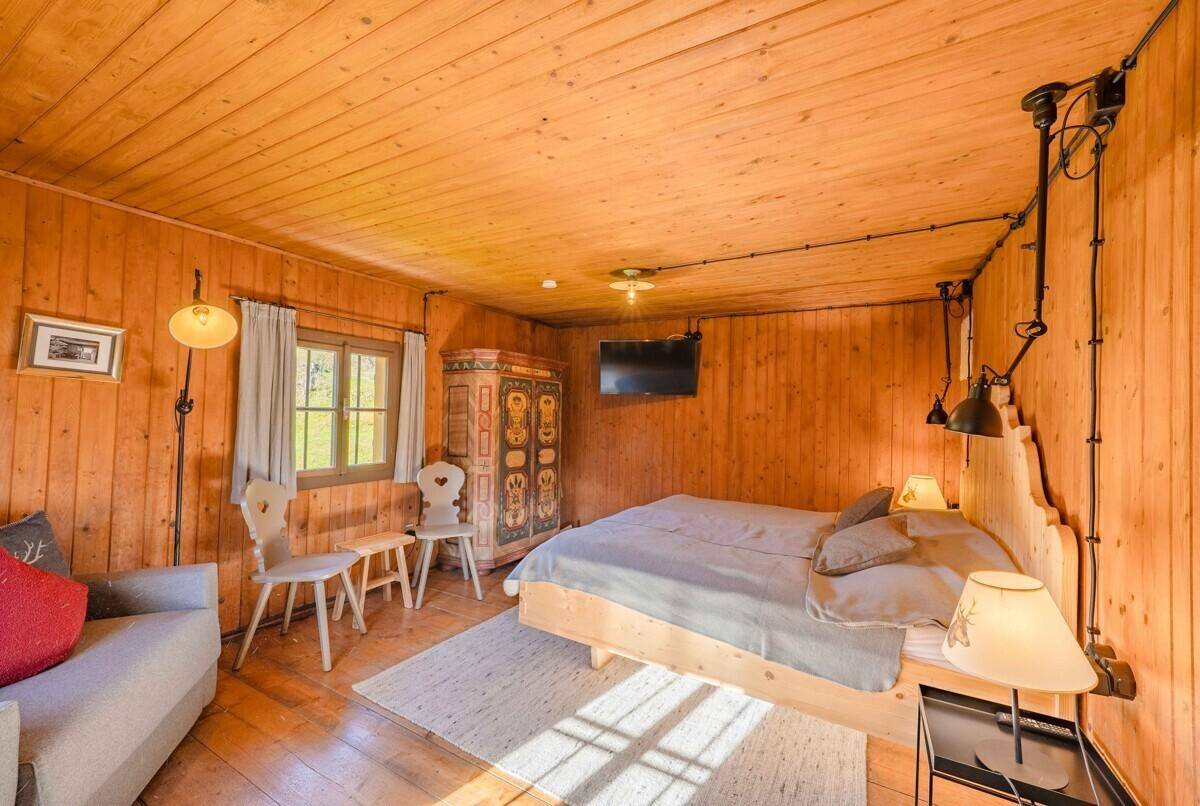 Helles Schlafzimmer mit Holzwänden, Holzboden und einem traditionell bemalten Kleiderschrank.