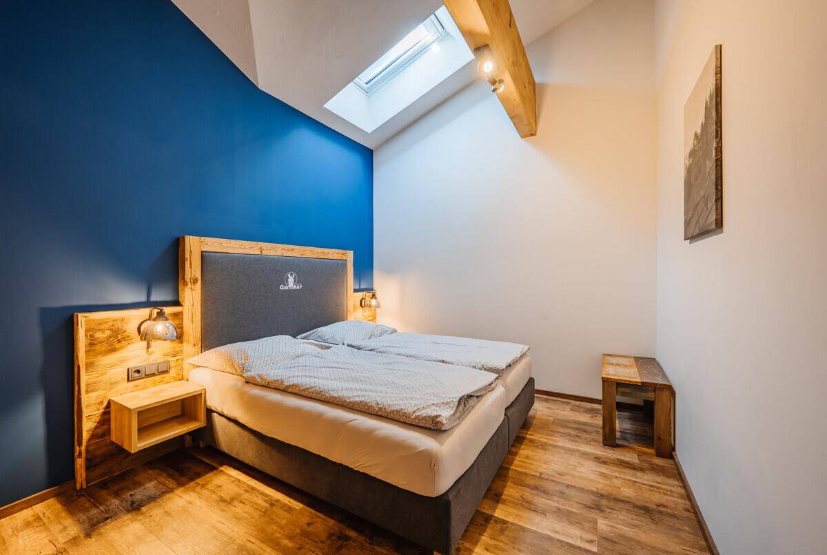 Helles Schlafzimmer mit Doppelbett, blauer Akzentwand und einem Dachfenster für viel Licht.