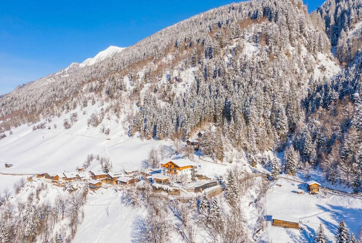 Weitläufige Luftaufnahme eines Gebäudekomplexes in einer tief verschneiten Berglandschaft mit Wäldern.