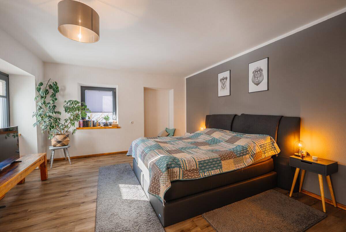 Großes Schlafzimmer mit Doppelbett, grauer Akzentwand, Holzboden und einem Fenster.