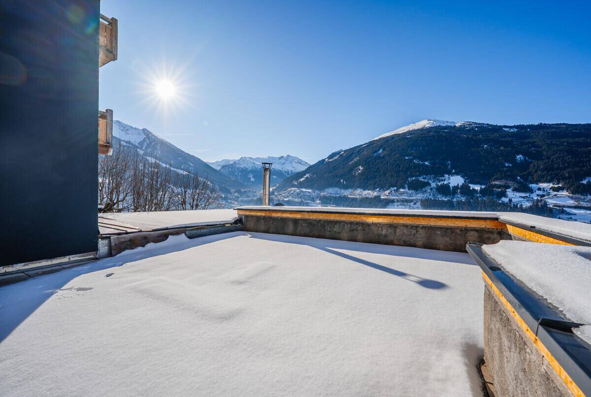 Verschneite Terrasse oder Flachdach mit weitem Blick auf die umliegende Berglandschaft im Winter.