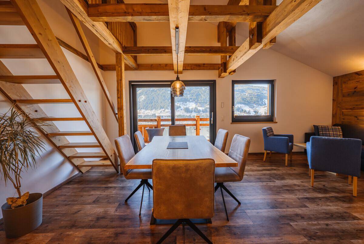 Heller Essbereich mit großem Holztisch, bequemen Stühlen und einer offenen Holztreppe.
