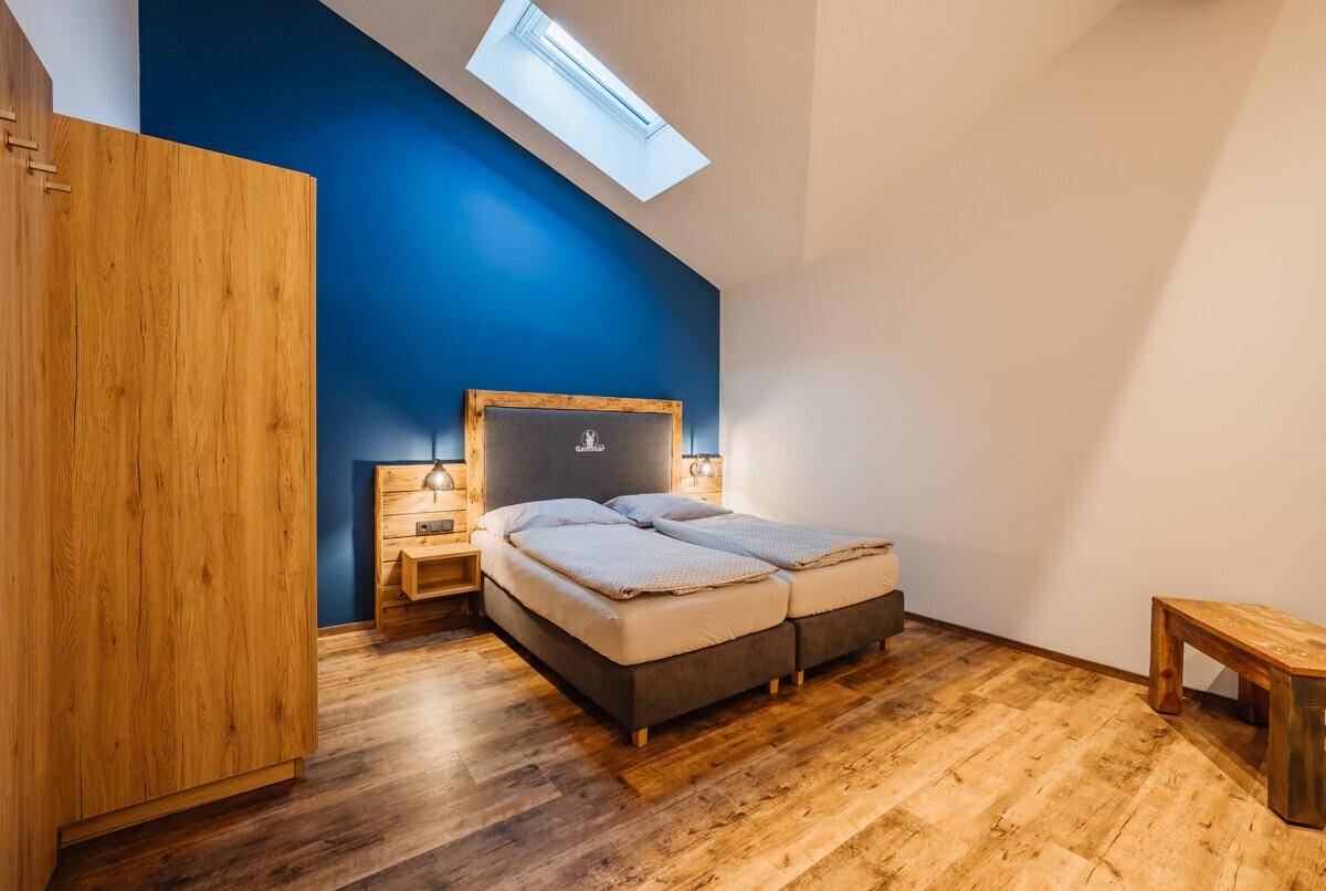 Schlafzimmer mit Doppelbett, Holzschrank, blauer Akzentwand und Dachfenster.