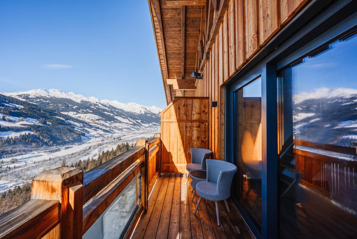 Geräumiger Balkon mit Holzgeländer und Glas, bietet weite Ausblicke auf die winterliche Berglandschaft.