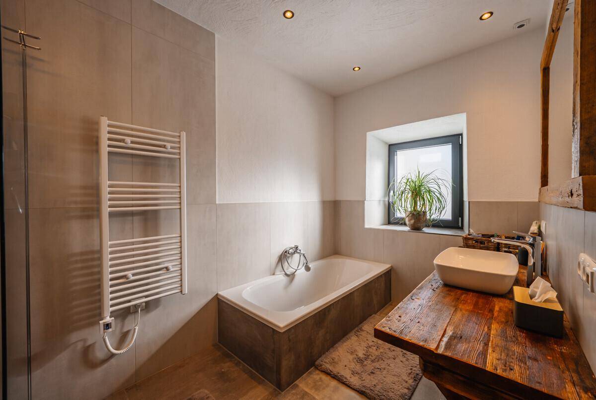Modernes Badezimmer mit Badewanne, Duschbereich, Holzwaschtisch und Handtuchheizkörper.