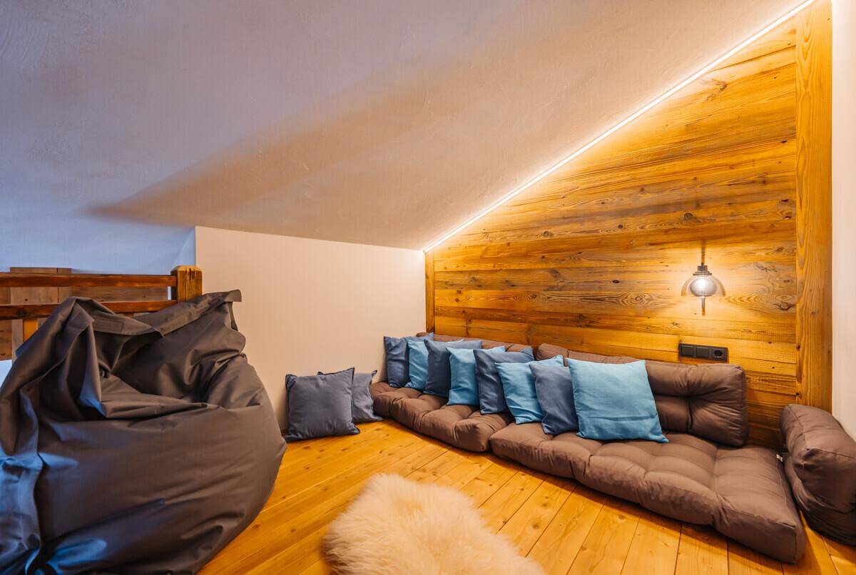 Gemütlicher Loungebereich unter einer Dachschräge mit Holzwänden und Bodenkissen.