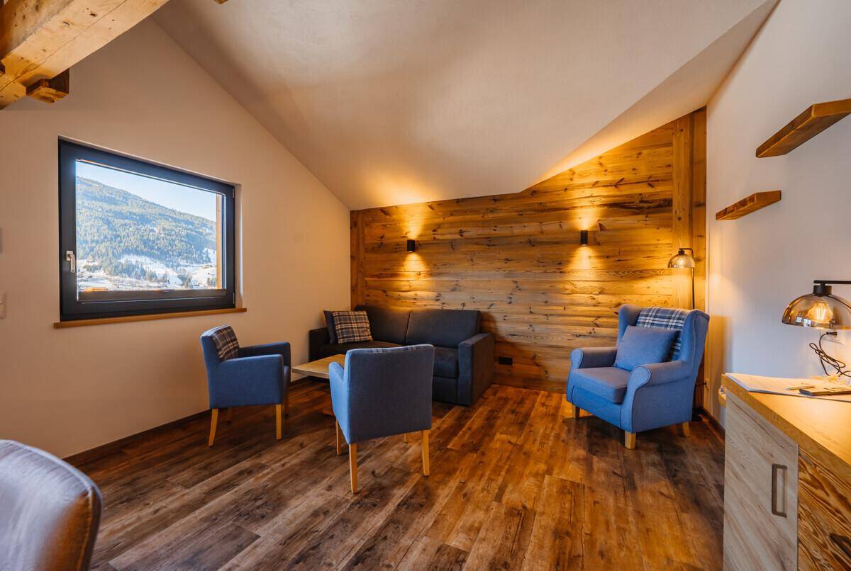 Wohnzimmer mit bequemen Sofas, Sesseln, Holzwandverkleidung und Blick auf die Berge.