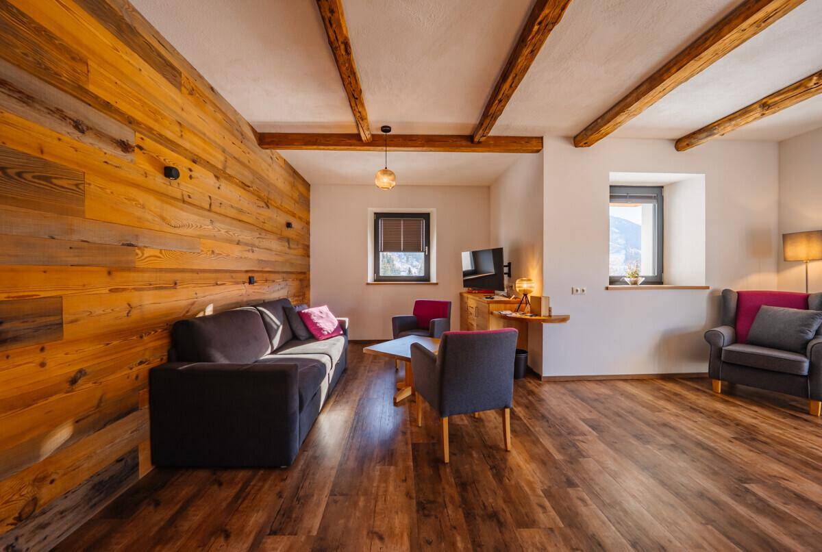 Geräumiges Wohnzimmer mit Holzwand, bequemen Sofas und Sesseln, sowie Holzbalken an der Decke.