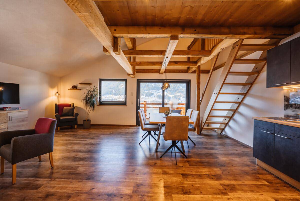Offener Wohnbereich mit Küche, Essbereich, Holzbalken und Zugang zu einem Balkon.