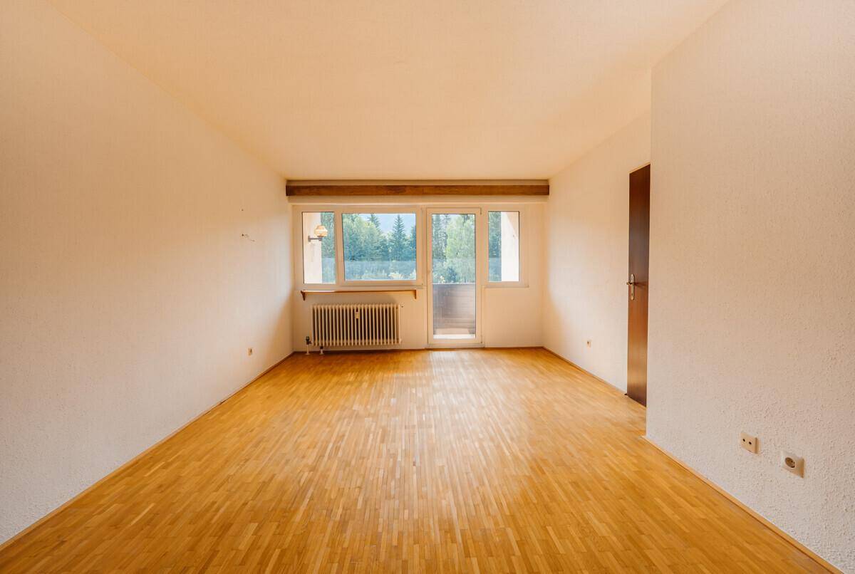 Geräumiges Wohnzimmer mit Parkettboden, Heizkörper und Zugang zu einem kleinen Balkon.