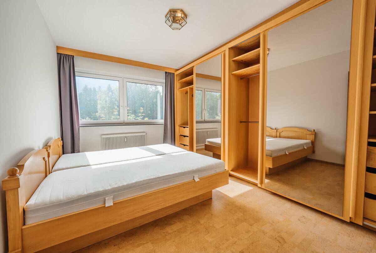Helles Schlafzimmer mit zwei Einzelbetten, Spiegelschränken und Korkboden, mit Blick ins Grüne.