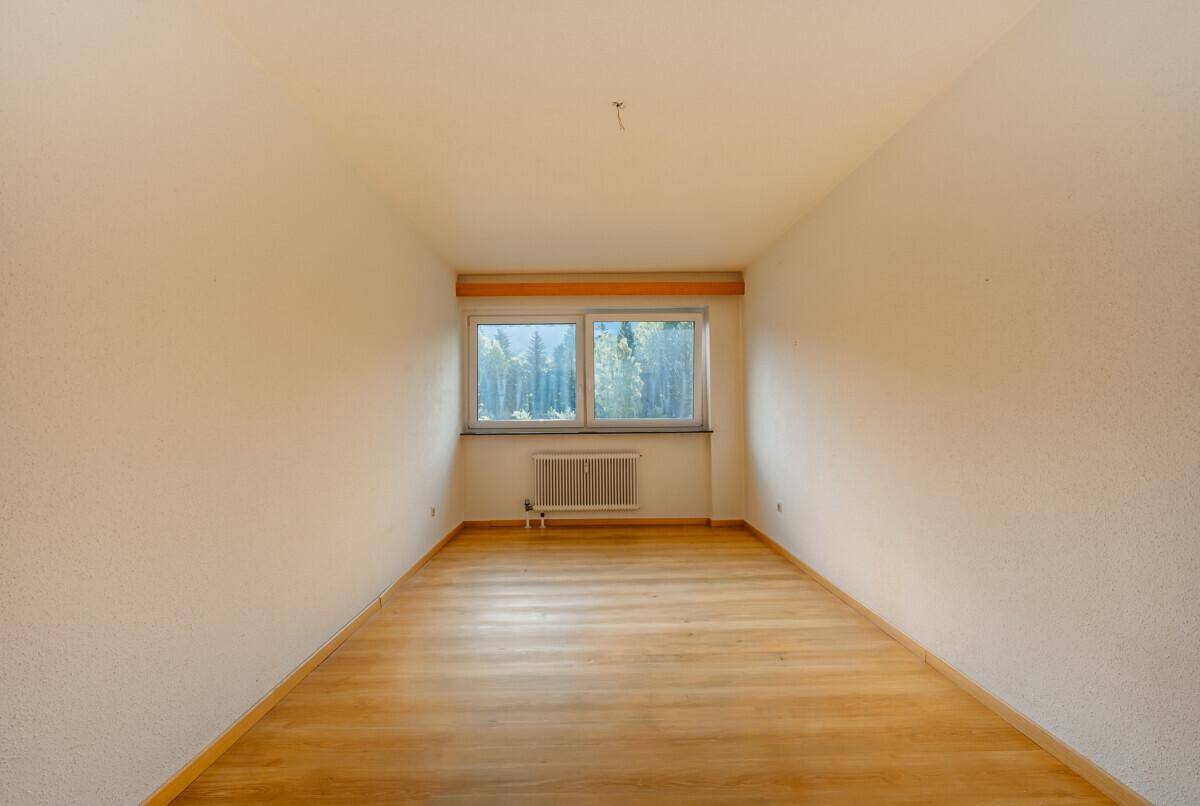 Helles Zimmer mit Parkettboden und Fensterblick auf die umliegende Natur und Bäume.