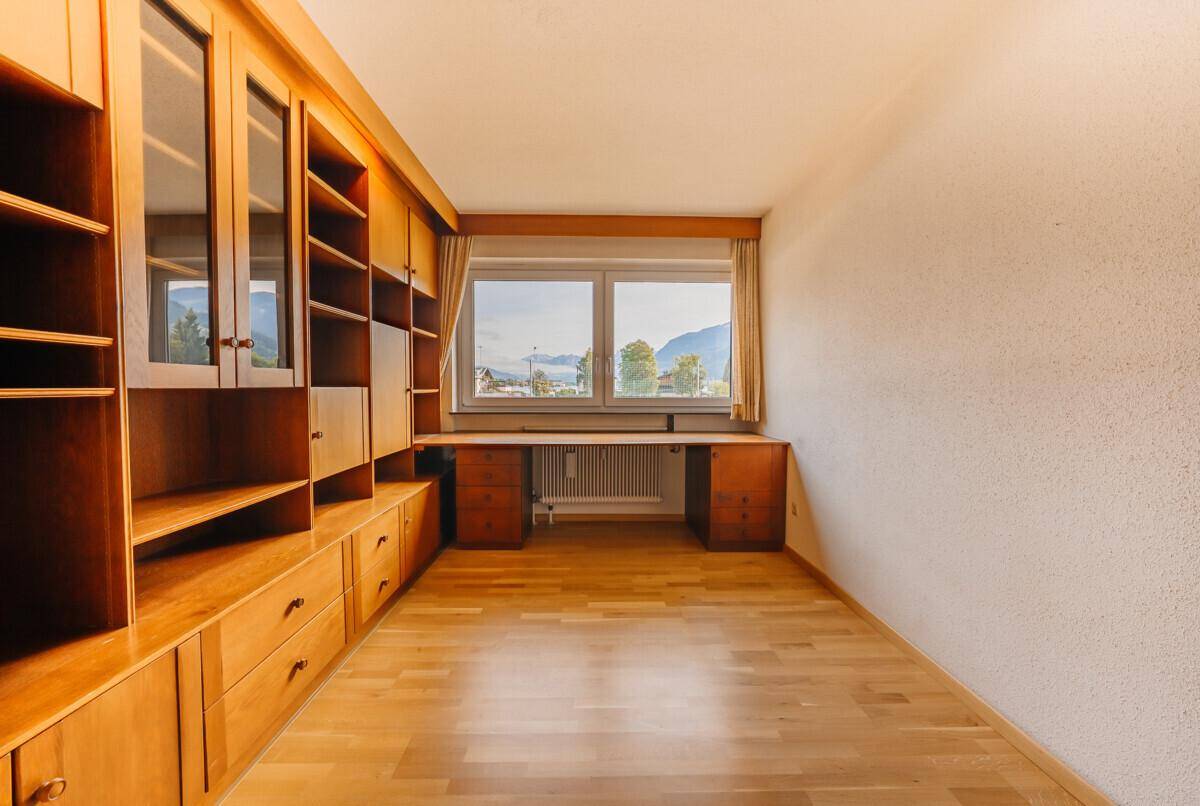 Geräumiges Zimmer mit Einbauregalen, Schreibtisch und Fensterblick auf die Berge und Natur.