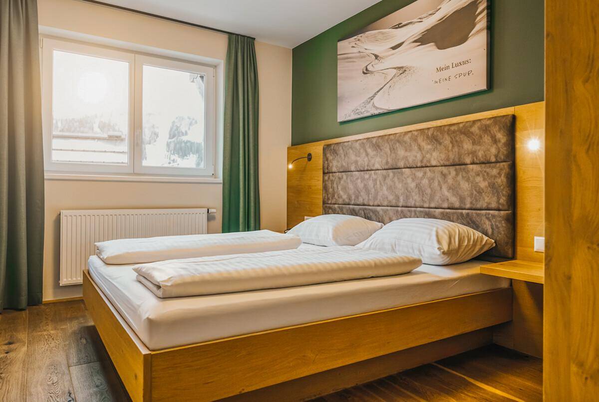 Helles Schlafzimmer mit Doppelbett, Holzboden und grüner Akzentwand, bietet eine gemütliche Atmosphäre.