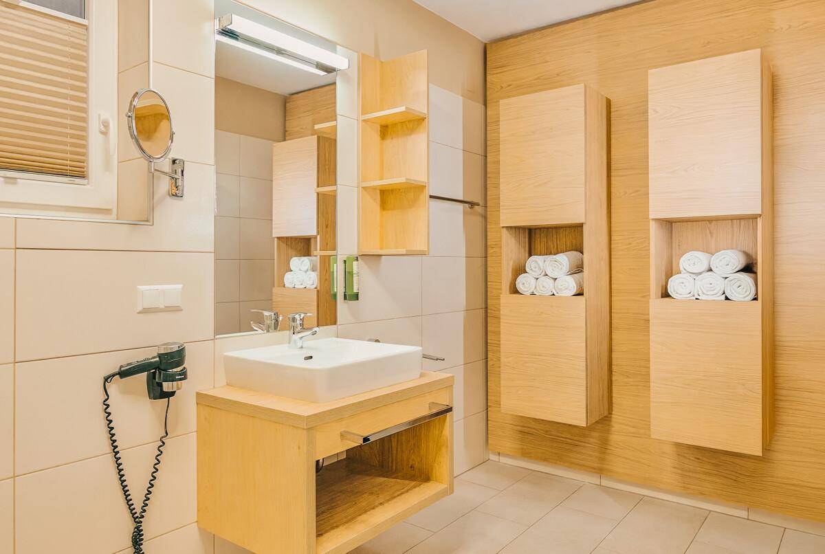 Modernes Badezimmer mit hellem Holzwaschtisch, Spiegelschrank und beigen Fliesen.