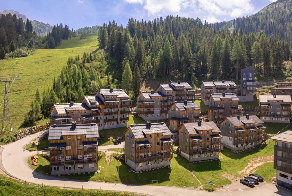 Eine Gruppe von modernen Chalets mit Holzbalkonen und Satteldächern in einer alpinen Umgebung.