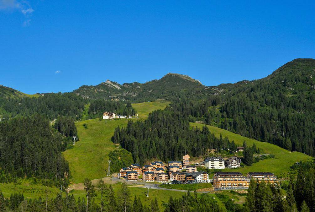 Panoramablick auf eine alpine Ferienanlage eingebettet in grüne Berglandschaft mit Wäldern und Wiesen.