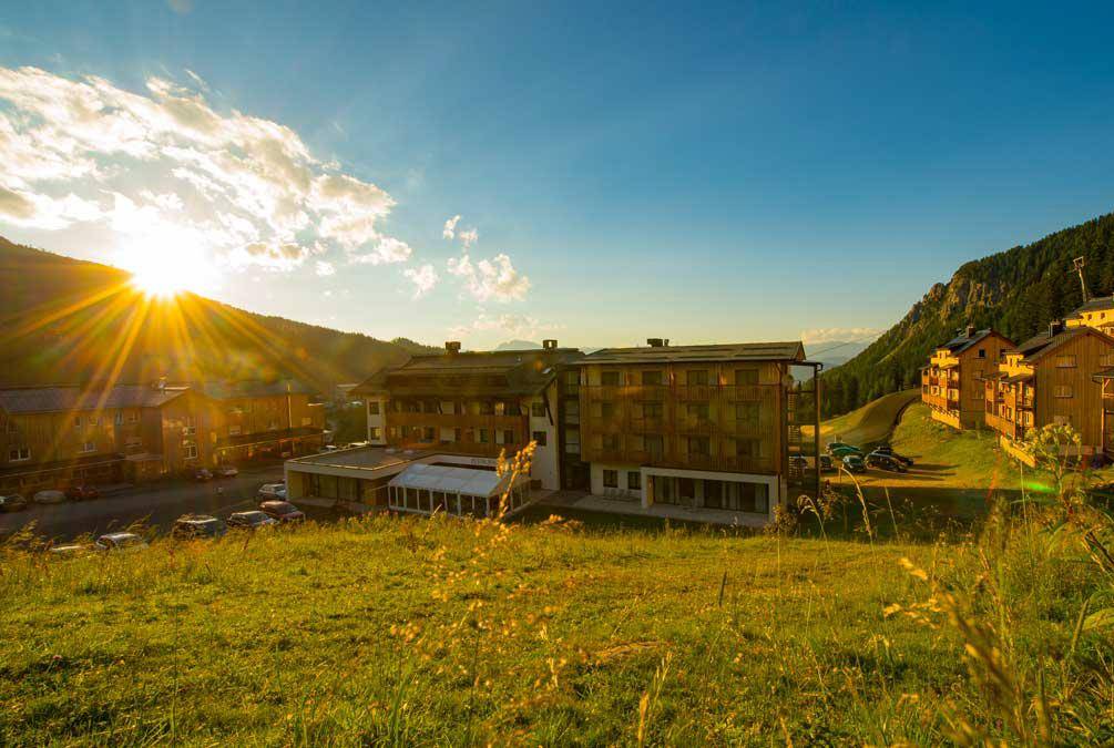 Ferienanlage in den Bergen bei Sonnenuntergang, umgeben von grünen Wiesen und Wäldern.