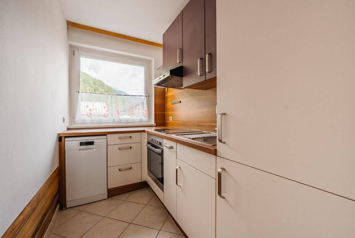 Funktionale Küche mit hellen Fronten, Fliesenboden und Fenster mit Bergblick.