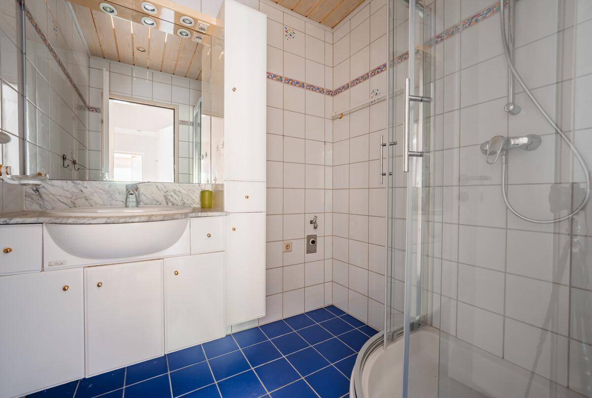 Badezimmer mit Dusche, Waschtisch und blauen Bodenfliesen in gutem Zustand.