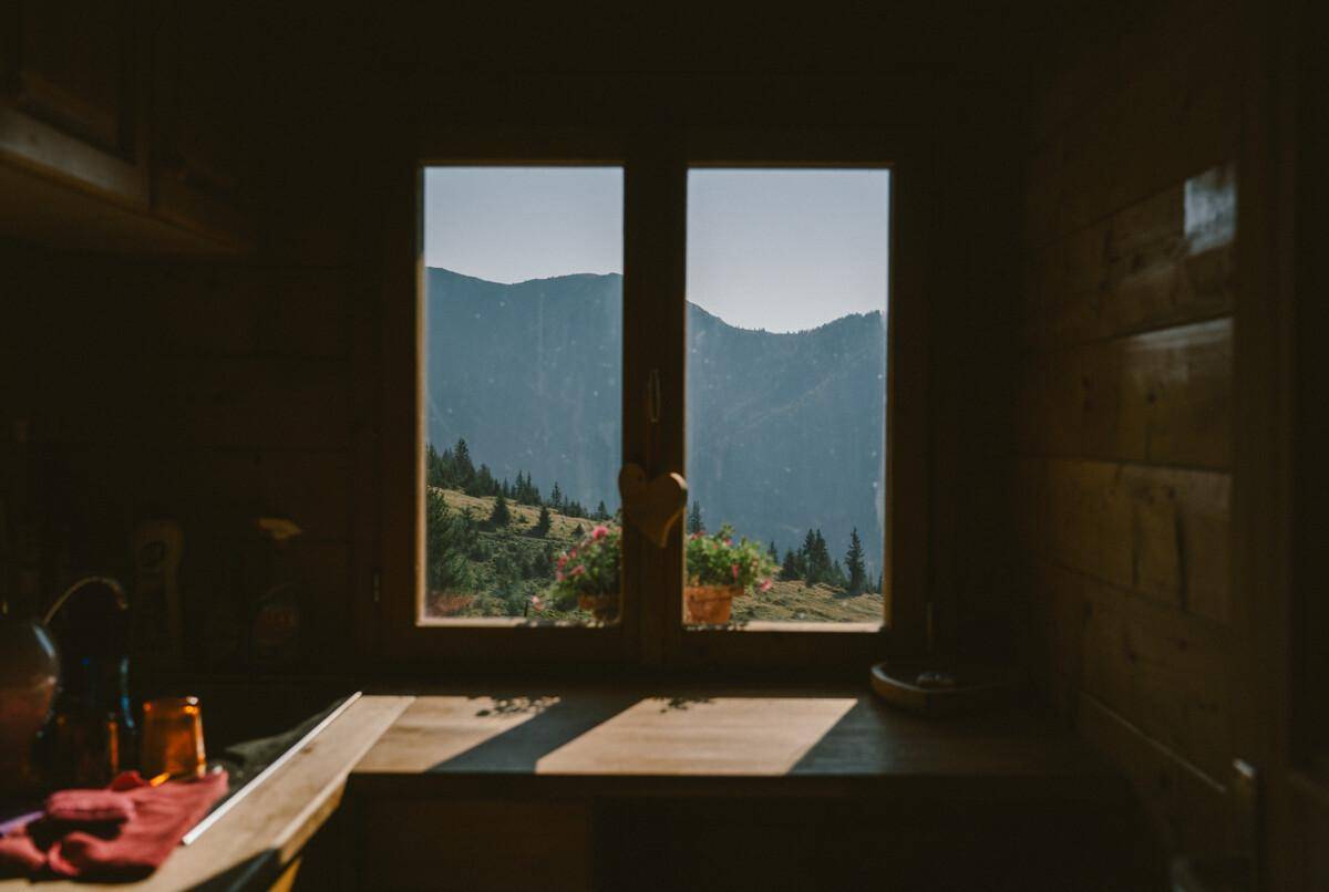 Fensterblick aus einer Holzhütte mit weitem Panoramablick auf die umliegenden Berge und Wälder.