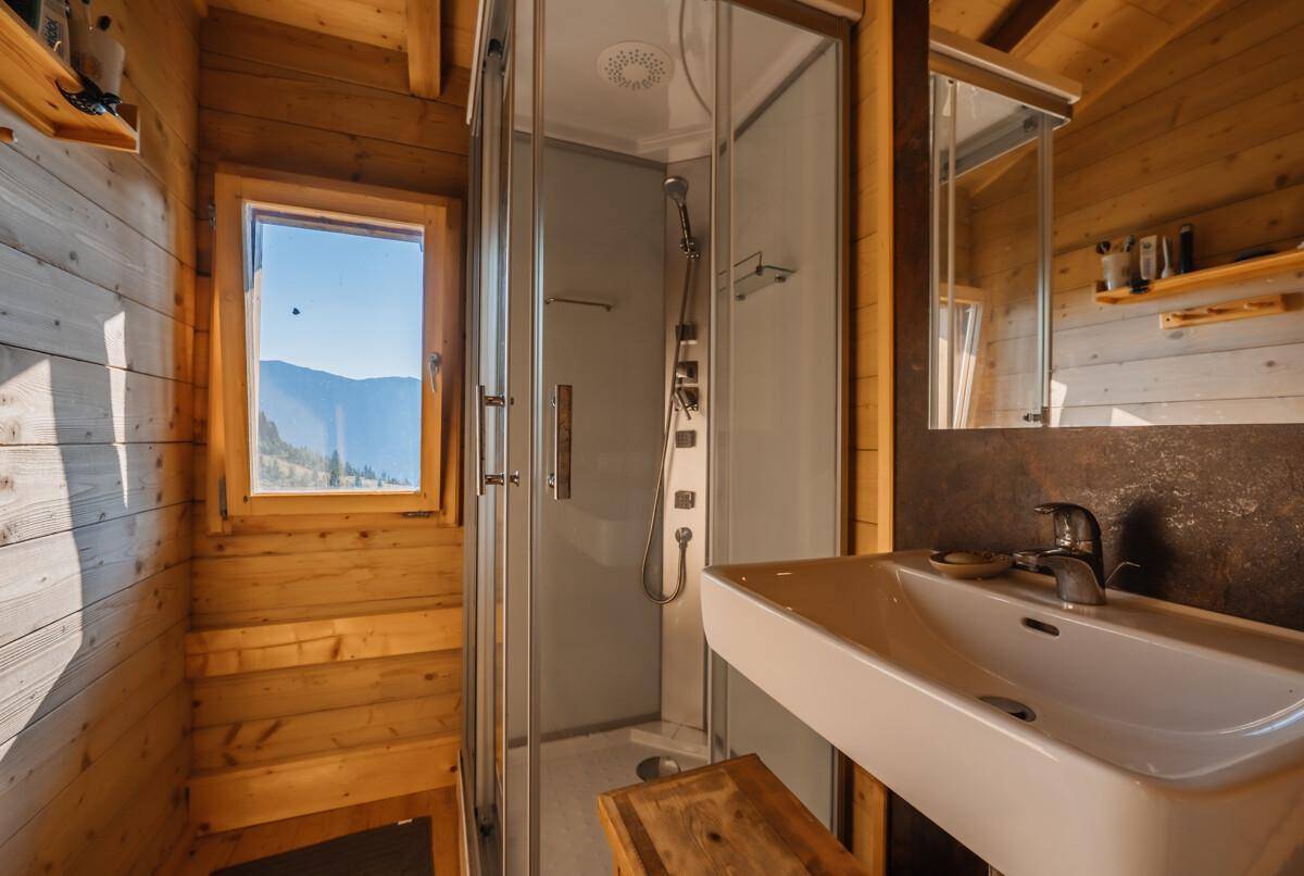 Rustikales Badezimmer mit Holzwänden, Dusche und Fenster mit Bergblick.