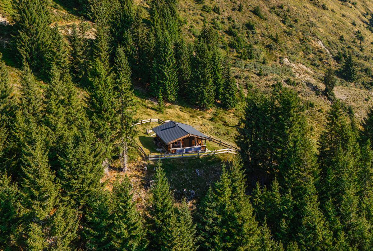 Luftaufnahme einer abgelegenen Holzhütte umgeben von dichten Wäldern und majestätischen Bergen.