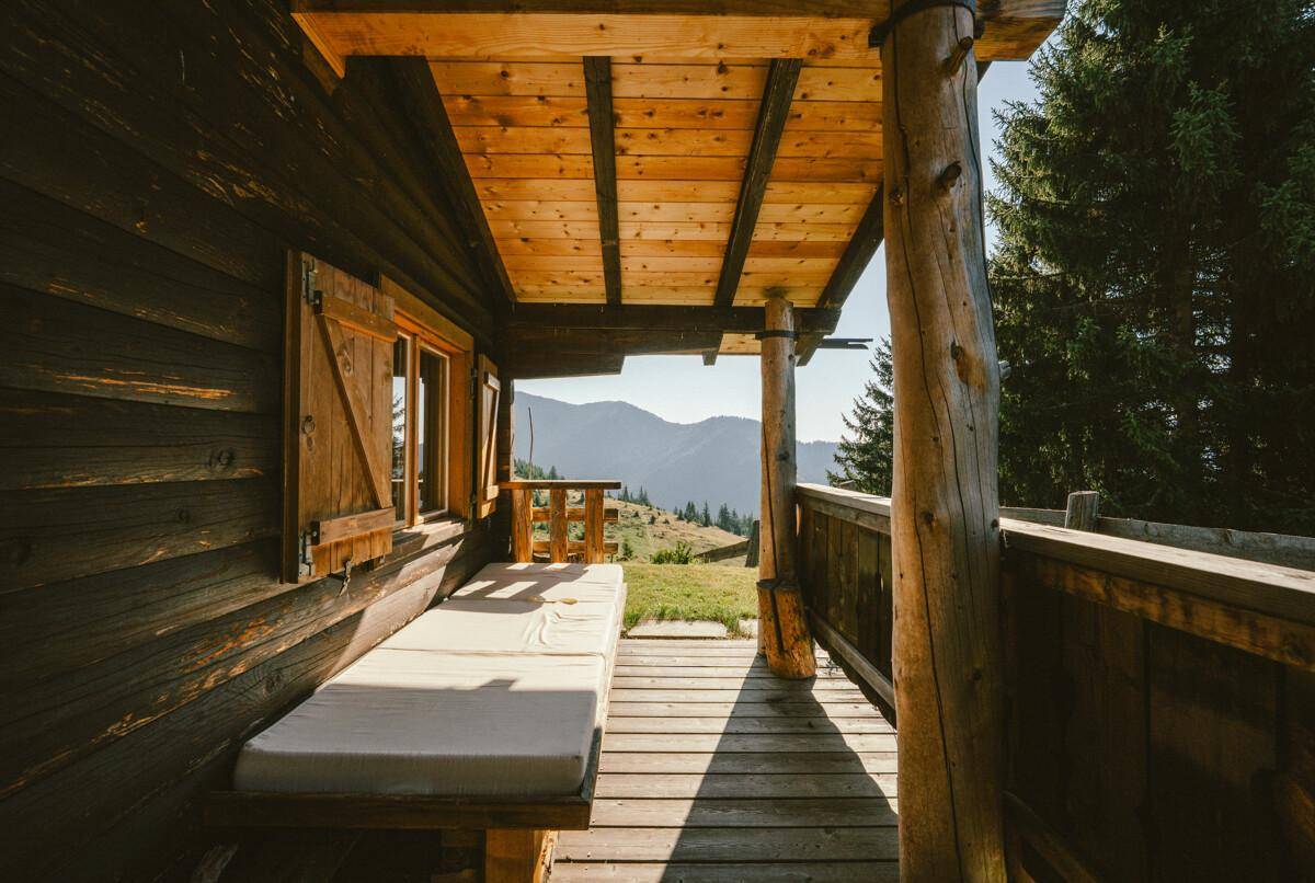 Überdachte Loggia mit Holzliege und weitem Blick auf die Berglandschaft unter blauem Himmel.