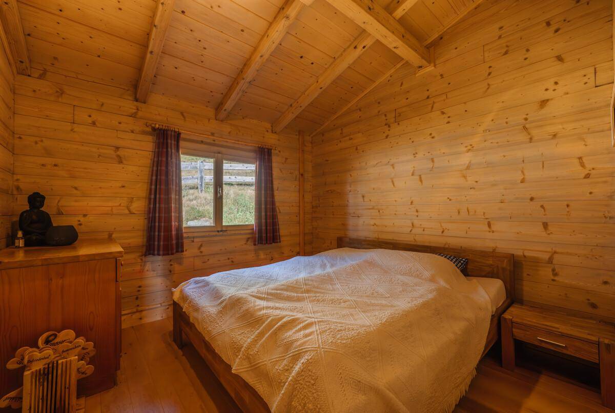 Schlafzimmer in einer Holzhütte mit Holzwänden, Holzboden und einem gemütlichen Doppelbett.